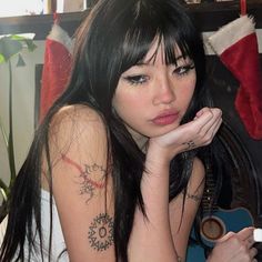 a woman with long black hair sitting next to a christmas tree