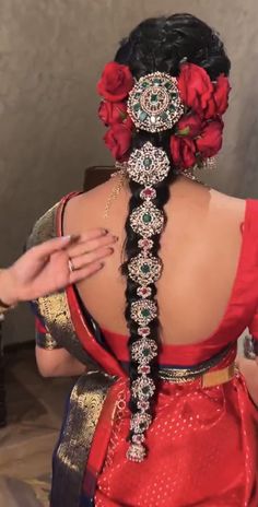 a woman in a red sari is braiding her hair into a flowered bun