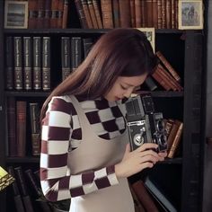 a woman holding an old fashioned camera in front of a book shelf filled with books