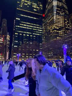 people skating on an ice rink in the city at night with skyscrapers behind them