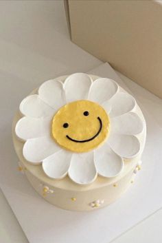 a white cake with a yellow smiley face on it's frosting and flowers