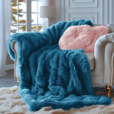 a white chair with a blue blanket and pink pillows on it in front of a window