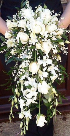 a woman holding a bouquet of white flowers in her hands and standing next to a door