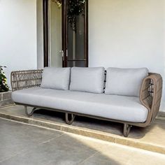 a white couch sitting on top of a stone floor next to a plant in a pot