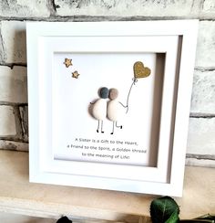 a white frame holding two rocks and a heart shaped balloon