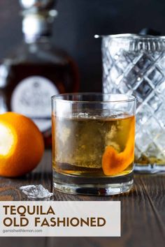 tequila old fashioned cocktail with an orange slice and ice cubes next to it on a wooden table