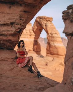 a woman in a red dress is sitting on a rock and posing for the camera