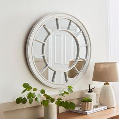 a white round mirror on the wall above a table with a lamp and potted plant