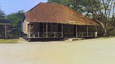 an old wooden building sitting in the middle of a dirt field next to some trees