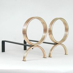 a pair of gold rings sitting on top of a black metal stand next to a white wall