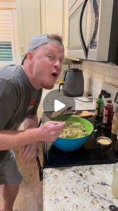 a man in grey shirt standing next to stove with bowl of food on top of it