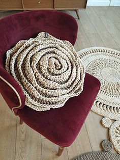 a red chair sitting on top of a wooden floor next to two crocheted rugs