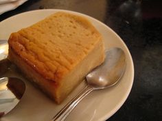 a piece of cake sitting on top of a white plate next to silver spoons