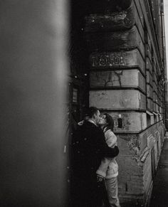 black and white photograph of two people kissing in front of a building on the street