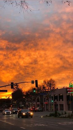 cars are driving down the street in front of an orange and blue sky at sunset