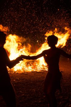 two people standing in front of a fire with their arms outstretched and hands out to each other