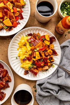 two plates with breakfast foods on them next to cups of coffee and condiments