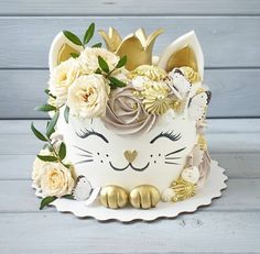 a white cat cake with gold decorations and flowers on the top is sitting on a table