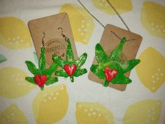 two earrings with green leaves and red hearts on them