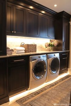 a washer and dryer in a room with dark wood cabinetry, lighting under the cabinets