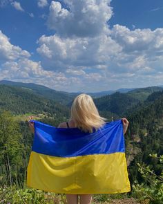 a woman holding a ukraine flag on top of a mountain