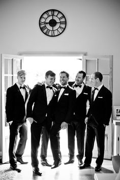 a group of men standing next to each other in front of a clock on the wall