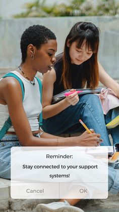 two young women sitting on the ground writing and looking at something in front of them