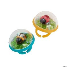 two plastic ladybugs sitting on top of green grass in a bowl with water