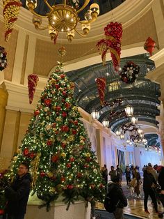 a christmas tree is in the middle of a lobby with lights and decorations hanging from the ceiling