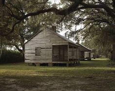 an old wooden house sitting in the middle of a field next to trees and grass