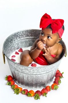 a baby sitting in a metal tub filled with milk and strawberries