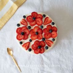 a cake with strawberries and blueberries on it next to a spoon, fork and napkin