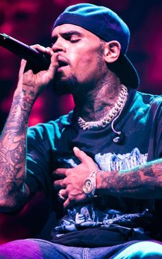 a man with tattoos on his arm holding a microphone in front of his face while sitting down