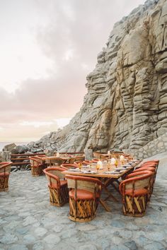 an outdoor dining area with tables and chairs next to a rocky cliff at sunset or dawn