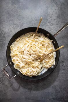 a skillet filled with noodles and two wooden spoons on top of a table