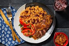 a white plate topped with meat, rice and veggies next to silverware