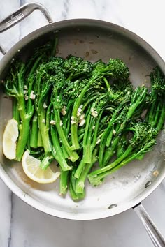 broccoli is being cooked in a pan with lemon wedges