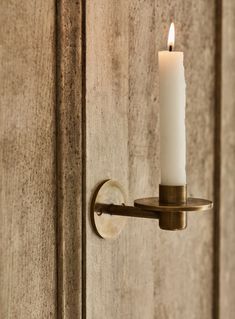 a candle is lit on the wall next to a wooden door with a metal hook