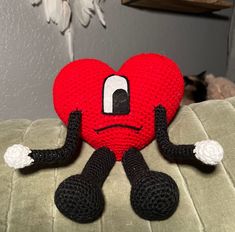 a crocheted heart with arms and legs sitting on a couch