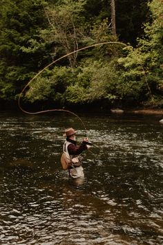 a man standing in the water while holding onto a fishing rod and wearing a hat