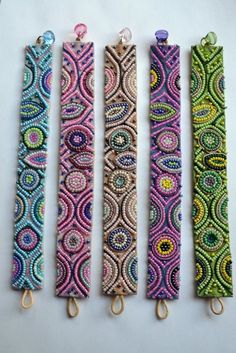 four different colored lanyards are lined up on a white surface, each with an intricate design