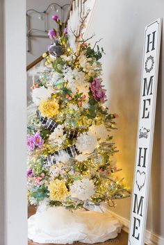 a decorated christmas tree with white and yellow flowers in the corner next to a sign that says home sweet