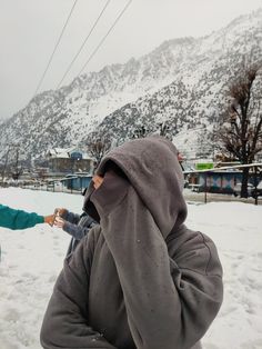 two people standing in the snow holding hands and talking on their cell phones with mountains in the background