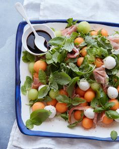 a blue and white plate topped with salad next to a bowl of dressing on top of a table