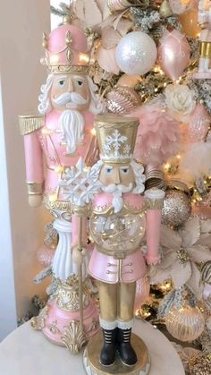 a pink and gold nutcracker next to a christmas tree with ornaments on it