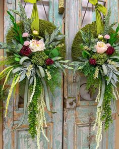 two wreaths with flowers and greenery hanging from the front of an old door