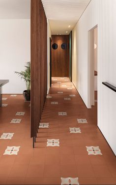 a long hallway with tiled flooring and wooden door leading to another room that has a potted plant on the far wall