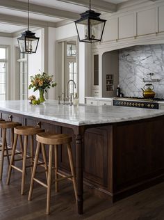 a kitchen island with three stools in front of it and two lights hanging from the ceiling