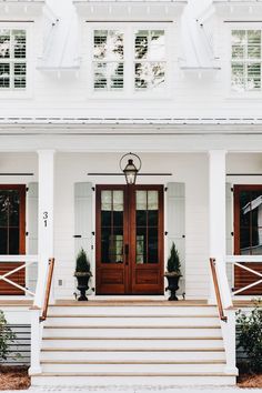 a white house with two brown doors and steps leading up to the front door that has potted plants on either side