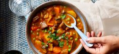 a person holding a spoon over a bowl of stew